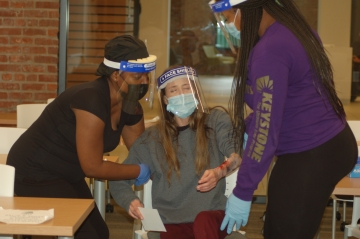 Two nursing students place a crisis actor in a chair bed during a disaster simulation exercise