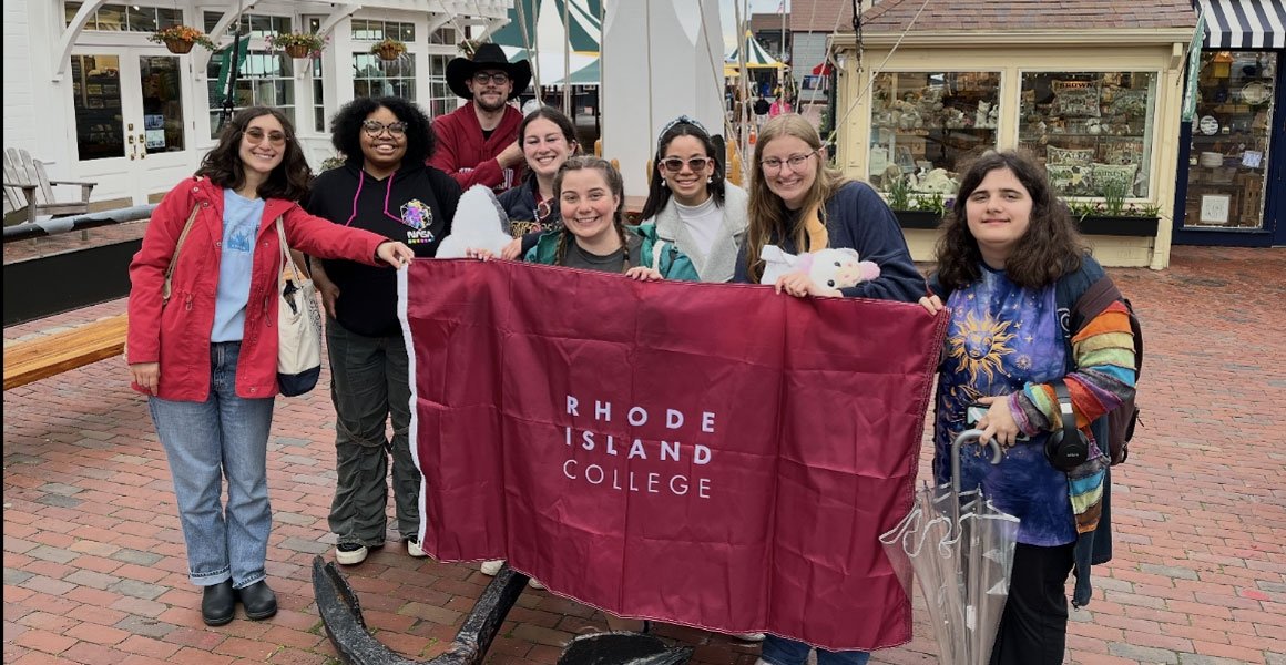 RIC students at Newport RI holding a burgundy RIC banner