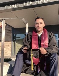 Jonathan sits on steps of Craig-Lee in his cap and gown