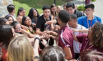 Students in huddle with hands in the center, together, at orientation