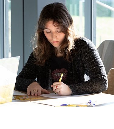 Student writing at table in sunlight