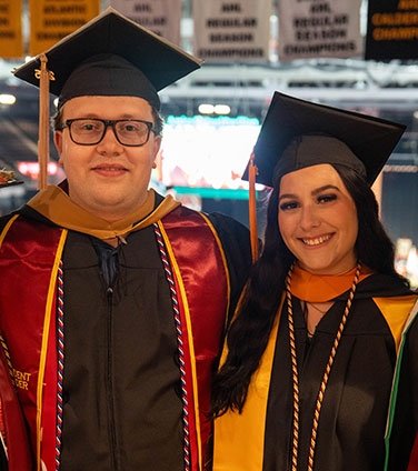 Two graduates standing together in cap and gown