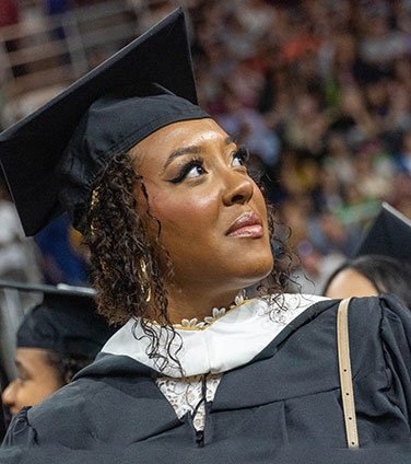 Grad in cap and gown looking up, proudly