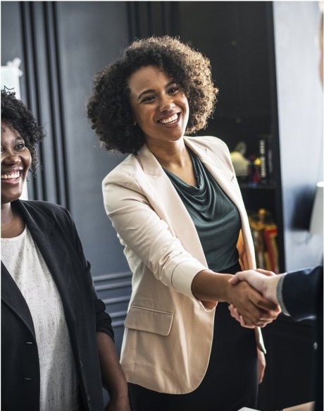 Two women shaking hands in man's office