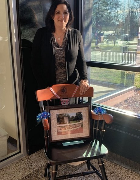 RIC alumnus Keri Rossi-D'entremont stands in front of a chair and plaque she was given as gifts by her colleagues