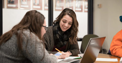 Two happy female students working on one laptop