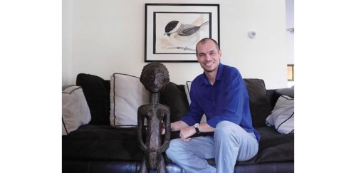 RIC alumnus Justin Bibee '12 sits with a sculpture of a human figure