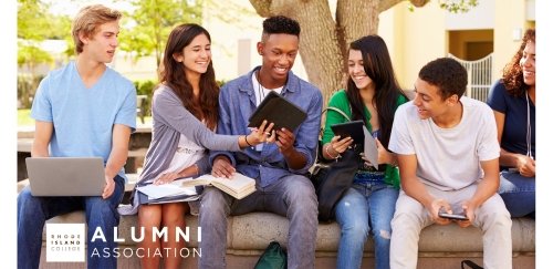 Students sitting outside together on a wall looking at tables, books, materials