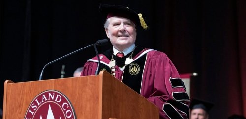 President Jack Warner, dressed in full academic regalia, speaks at a podium during Commencement