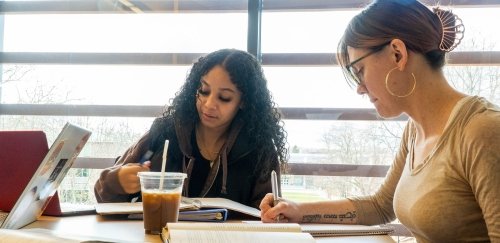 Math students working together at a table with notebooks, laptop, coffee