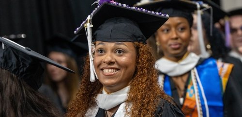 Smiling graduate in regalia amongst crowd