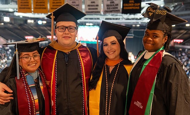 Four students standing together in cap and gown at commencement