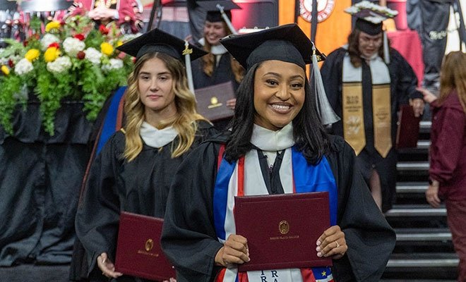 Graduates coming off of the stage with diplomas