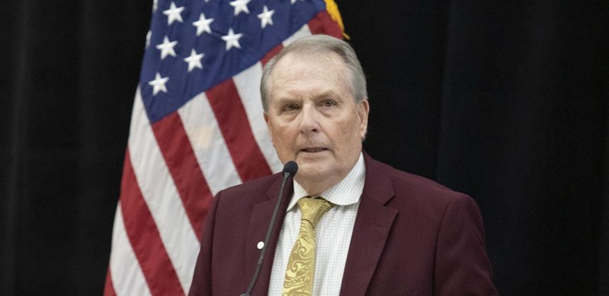 President Warner at microphone with American flag behind him